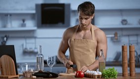 shirtless man in apron cooking in kitchen and drinking white wine