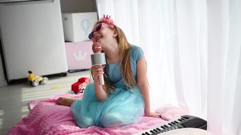  Beautiful little girl in a princess costume sings into a karaoke microphone.  Stay at home