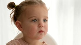 Cute baby girl sitting on chair and watching cartoon at home close-up