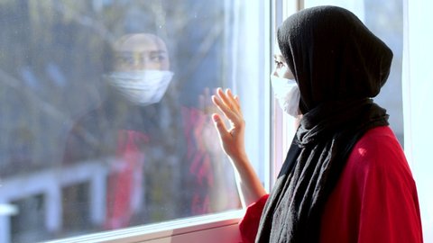 COVID-19 Pandemic Coronavirus Woman with hijab with wearing face mask looks out the window isolation. arab woman hijab. Muslim woman with hijab arab.