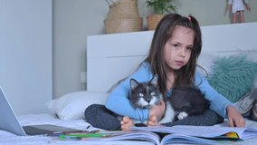Distance learning online education. Schoolgirl  with digital tablet laptop notebook and doing school homework. Sitting on bed with training books. Home school. Tender relationship with a pet cat. 4k 