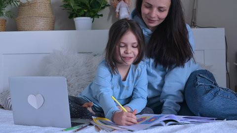 Distance learning online education. Schoolgirl  with digital tablet laptop notebook and doing school homework. Mom does homework with her daughter at home in bed. Friendship with children