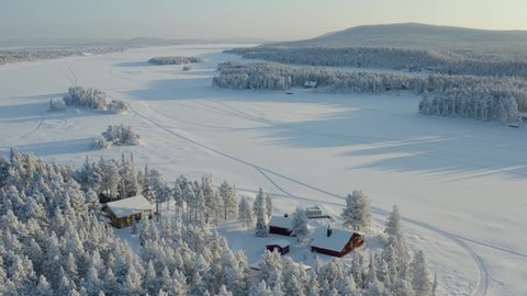 Aerial drone shot of a frozen lake, blocks of ice, frozen trees, reflections, typical house during the winter of polar Lapland.