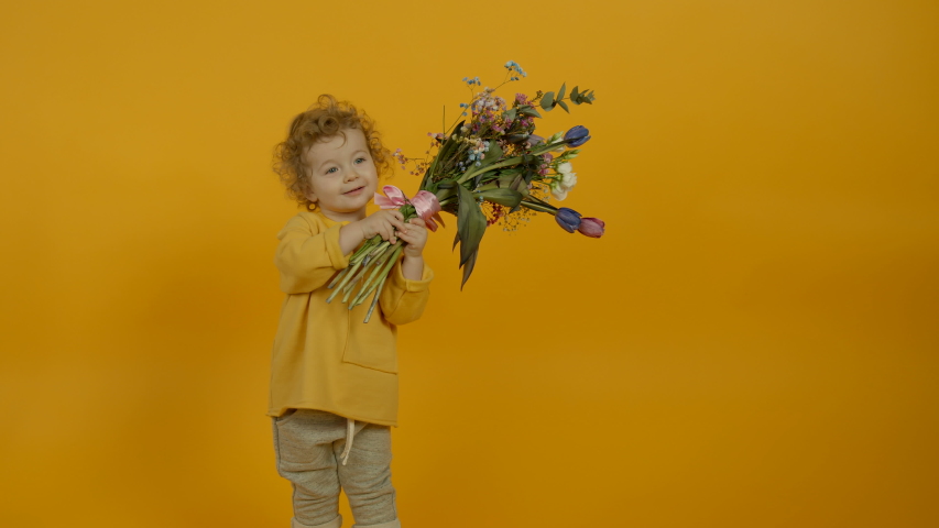 Smiling child holding flowers and dancing on yellow background