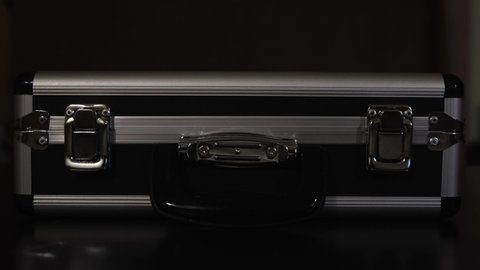 Close up of female hands opening silver metal suitcase with locking system. Concept. Opening aluminum carrying case to find shining mysterious object inside.