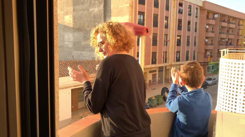 A Spanish woman and her son applaud from the balcony of their apartment for the COVID 19 pandemic health team. | Shutterstock HD Video #1050081400