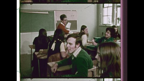 1970's A Teacher teaches a Lesson in a Rowdy Classroom. From a Window a Student Throws a Paper Airplane hitting the Teacher in her Perm. 4K Overscan of 16mm Film Showing Frame Lines and Sprocket Holes
