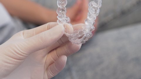 tight close-up of gloved hand holding two invisalign aligners, with patient in the background