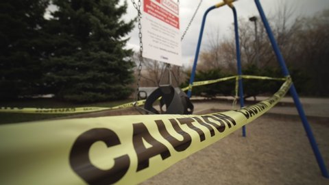 Toronto, Ontario, Canada - April 7, 2020 : Swing set abandoned and locked due COVID-19 coronavirus alert closure, all parks amenities, including, playgrounds, are closed. Yellow caution tape wrapped.