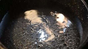 Slow motion clip of water boiling in a pot with bubbles breaking on surface