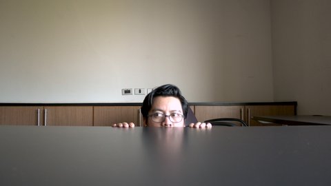 Asian male climb up behind the desk suspiciously like making a mistake Or stealing things in the office