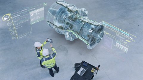 Industry 4.0 Factory: Two Engineers Uses Digital Tablet Computer with Augmented Reality Software to Connect with High-Tech CNC Machinery, Robot Arm and Visualize Maintenance. Elevated Shot