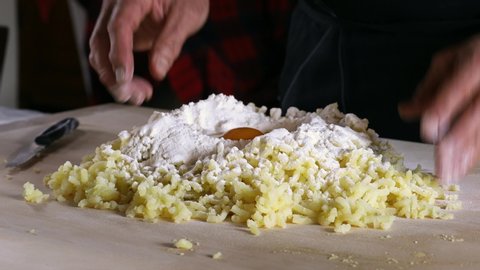 Chef's hands making home made potato gnocchi. Breaking an egg with a fork in the boiled and mashed potatoes. Italian cuisine, regional specialty, genuine recipe. 
