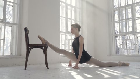 Ballerina doing te splits on the chair. Indoors, at the ballet studio. Handheld shot.