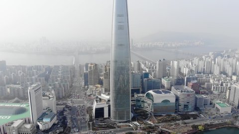 SEOUL, SOUTH KOREA - MARCH 29, 2018: Scenic aerial perspective of Lotte World Premium Tower and surroundings, camera fly back. Smog in the air, cityscape and Han River on background dissolve in mist