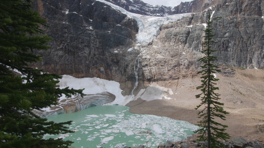 Static shot of Angel Glacier melting into a lake below at Mt Edith Cavell in Japser with pine trees in the foreground