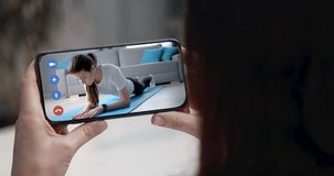 Close up of female hands holding smartphone during video chat with sport instructor that giving advices for exercising at home. Woman workout remotely at own apartment.