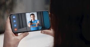 Back view of young girl watching video instruction from female coach on smartphone. Distance training during video chat at home. Concept of active lifestyle.