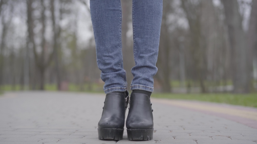 Camera moving up from feet to face of slim beautiful Caucasian woman standing on park alley wearing protective face mask. Portrait of brunette girl spending day outdoors on Covid-19 quarantine.