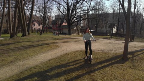 girl with long hair rides black electric scooter in park