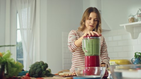 Beautiful Young Female Preparing a Healthy Green Smoothie in a Blender. Authentic Stylish Kitchen with Healthy Vegetables. Natural Clean Products from Organic Farming Used to Make Drinks.