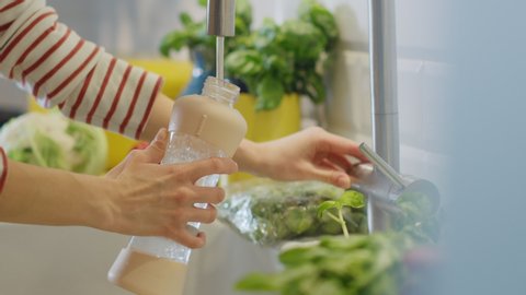 Close Up Footage of a Woman Filling a Reusable Plastic Bottle with Clean Filtered Tap Water. Using Sports Bottle for H2O in a Modern Kitchen. Natural Clean Diet and Healthy Way of Life Concept.