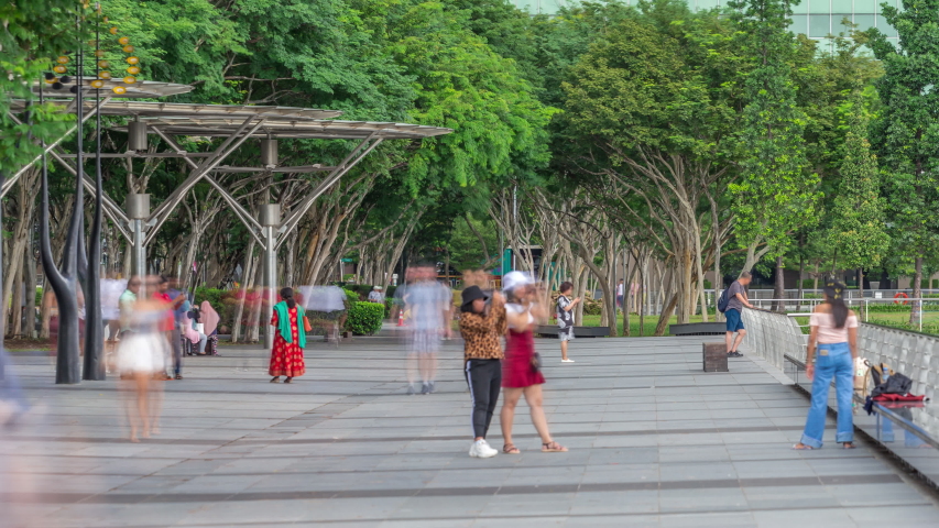 Walk way with trees and bench beside at parks and outdoor of marina bay with singapore skyscrapers skyline timelapse. View from shopping mall