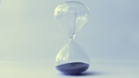 Hourglass with black sand being flipped with hand