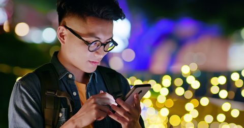 asian young man use smart phone outdoor and play interesting mobile game in the evening