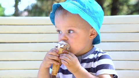 Little kid boy licking ice cream in a waffle cone at summertime in the park. Portrait of three years old child with blue eyes, who feel happy and eating ice.
