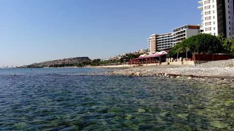 Low Flying Beach Side Drone Shot Scanning Across the Rocks and Shore with Pedestrians, Hotels, Beach, and More in View in Limassol, Cyprus
