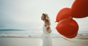 Beautiful woman in a white dress walking on the beach holding red balloons, endless childhood freedom concept