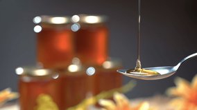 Thick honey dipping on metal spoon, golden liquid honey flowing. Honey jars on grey background, natural product and beekeeping concept. Healthy nutrition