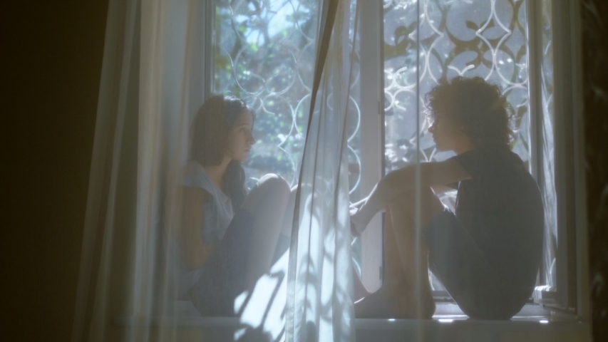 teenage brother and sister are sitting on the windowsill behind the tulle