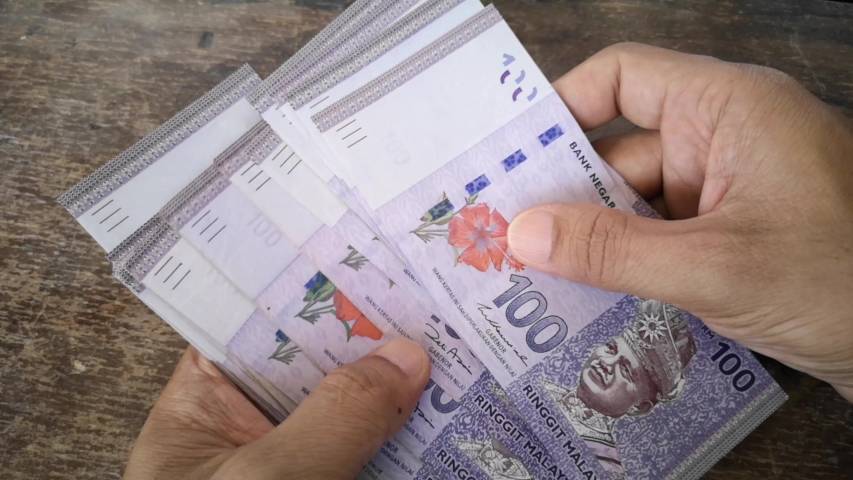 Hand calculates the banknote Ringgit Malaysia, value of the 100 on the wooden table. (selected focus) | Shutterstock HD Video #1050176386