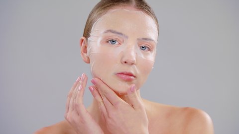 Close Up Beauty Portrait Of Young Caucasian Blonde Woman With Blue Eyes She Applying Finger White Paper Tissue Sheet Mask On Face On Gray Background Skin Care Concept Slow Motion