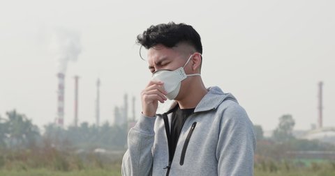 asian man coughs and wears protective n95 mask because air pollution standing in front of factory
