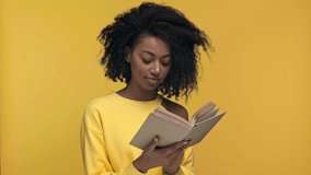 smiling african american woman reading book isolated on yellow