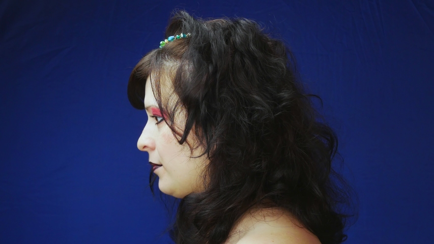 The girl laughs.Dark matted hair with beads.Brown eyes and black lips.Bright red makeup.Closeup on blue background.The image of witches.