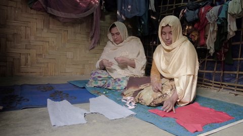 Teknaf, Bangladesh - November 2018: Two Rohingya women are hand sewing fabric in their shelter home in Teknaf refugee camp, Bangladesh