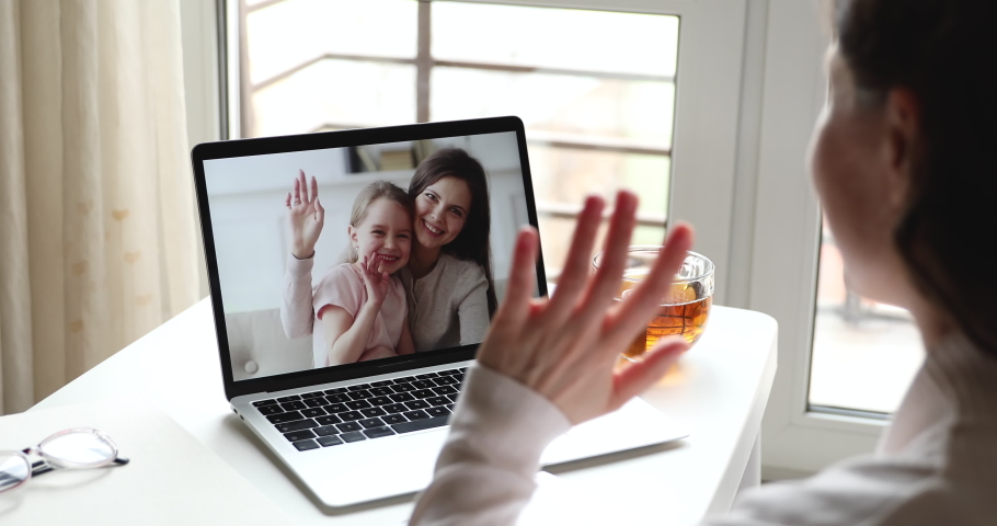 Young woman mom video calling on laptop talking by webcam with happy child daughter and babysitter on computer screen sits at home table. Videocall, family chat concept. Over shoulder close up view Royalty-Free Stock Footage #1050218956