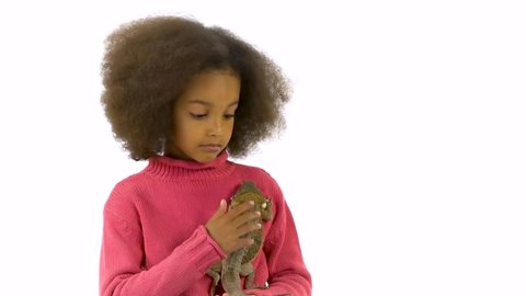 Little african curly girl is holding and stroking Bearded agama at white background. Slow motion
