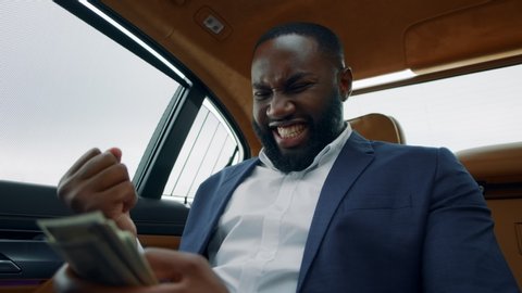 Closeup black man counting money cash at luxury car. Successful african business man celebrating victory at backseat. Excited afro man holding cash money in hands at vehicle.