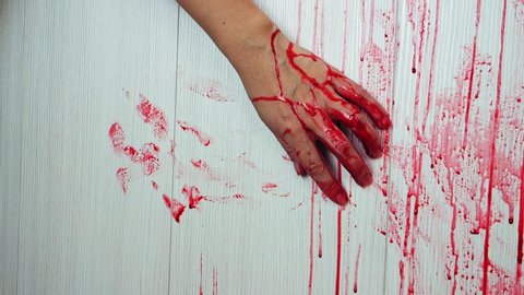 Blood flow on the wall, a human in danger. A female hand reaches out, holding on to the wall, leaving a trace of blood on the wall.