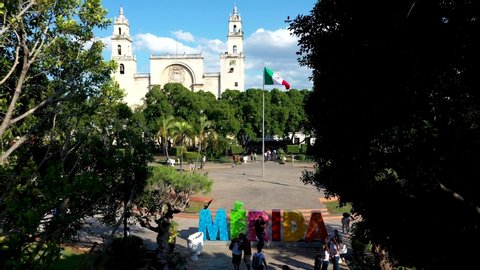 Merida, Mexico - 01 23 2020: Aerial view through trees from the Merida tourist sign across the zocalo, plaza grande to the cathedral san ildefonso in Merida, Yucatan, Mexico.