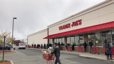 Staten Island, New York / United States - April 10 2020: COVID-19 social distancing. People wait on very long line outside Trader Joe's supermarket. People wearing masks and face coverings.