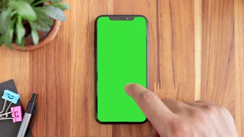 Thailand, Roi-Ed - Apr 3, 2020 : Smart phone place on table wood with green screen, Close-up the cell phone is on the brown desktop, Man's finger slide Up or Down display mobile phone with chroma key.