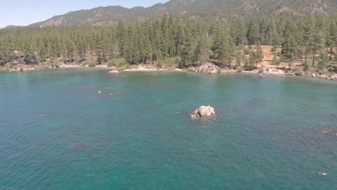 Lake Tahoe, NV/USA - August 24, 2019:  Swimmers hang out on a tiny rock island emerging from Lake Tahoe's crystal clear blue water. Beautiful summer day on the lake during family vacation.
