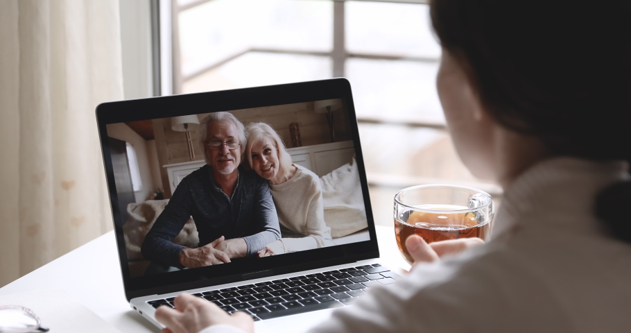 Over shoulder closeup view of young woman daughter video calling old senior parents talking with grandparents mom dad in webcam conference chat app on laptop screen on table. Family videocall concept.