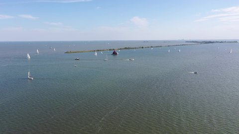 4k drone aerial footage of sailing sail boats of the dutch shore near the city village of Volendam. wealthy lifestyle recreation. on a sunny but windy day. traditional boat with red sail. netherlands